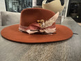 Load image into Gallery viewer, Burnt orange flat brim hat with coral pinks and creams hand tied embellishments and dried florals. This hat bar was at a Private event.