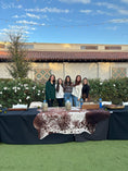 Load image into Gallery viewer, The Harper and Honey Team Picture behind their branding bar setup with cowhide across the table and all their branding tools.