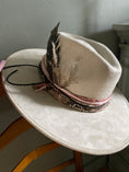 Load image into Gallery viewer, Elevate your style with The Bre, an ivory flat brim rancher hat crafted from vegan suede, featuring a striking snake skin print, blush-tone recycled silk from India, and finished with a feather and sun brand. Shop now at Harper & Honey for a chic and unique statement piece!