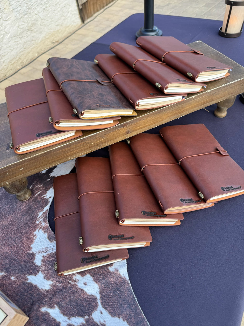 Collection of brown leather journals on a wooden table outdoors.