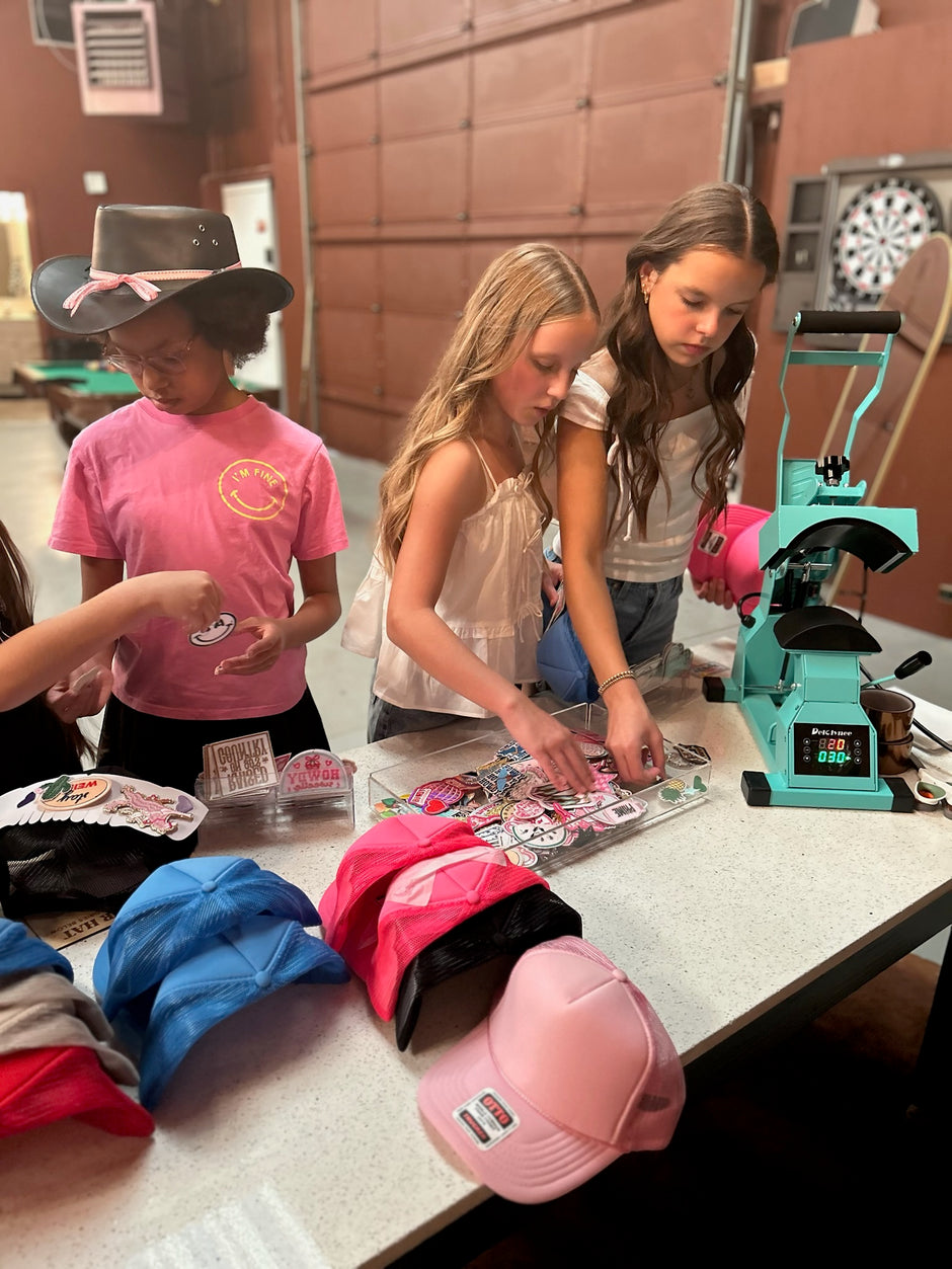 Children working on a craft project with hats and a teal machine in a vintage garage setting.